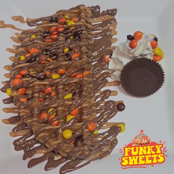 Waffle covered in chocolate and peanut butter drizzle, Reese's Pieces, with whipped cream and a peanut butter cup.